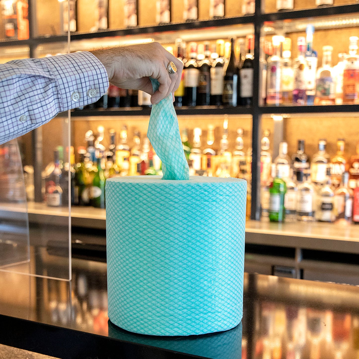 Person holding a green roll of Robert Scott handy wipe towel in a bar setting with shelves of bottles.